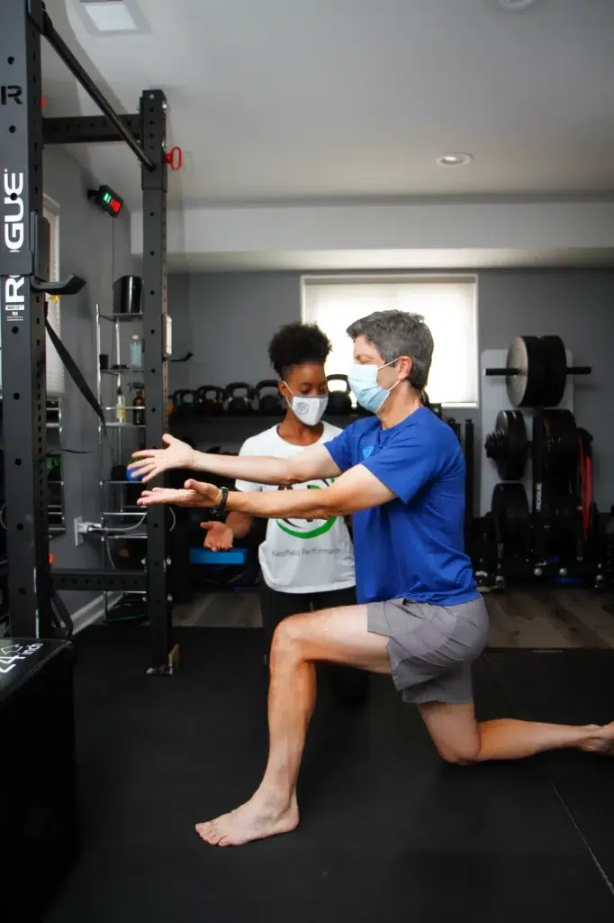 Two men exercising with resistance bands in a gym while wearing masks.