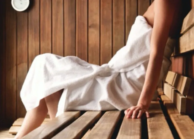 Person relaxing in a sauna wrapped in a white towel.