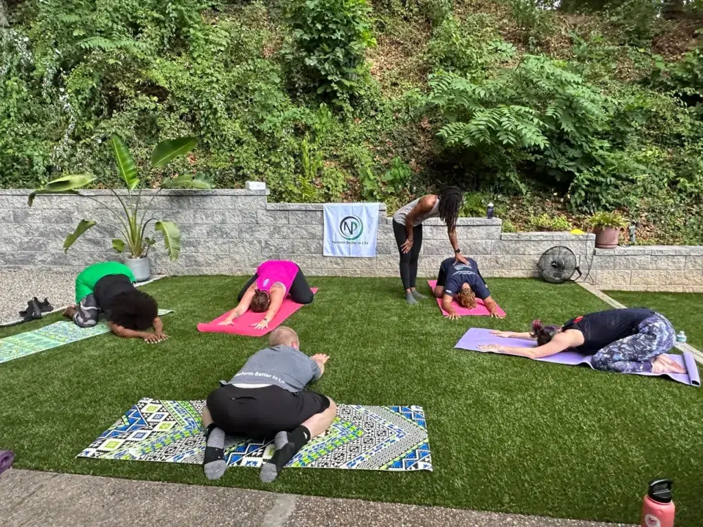 Group yoga session outdoors with participants in various poses on mats.