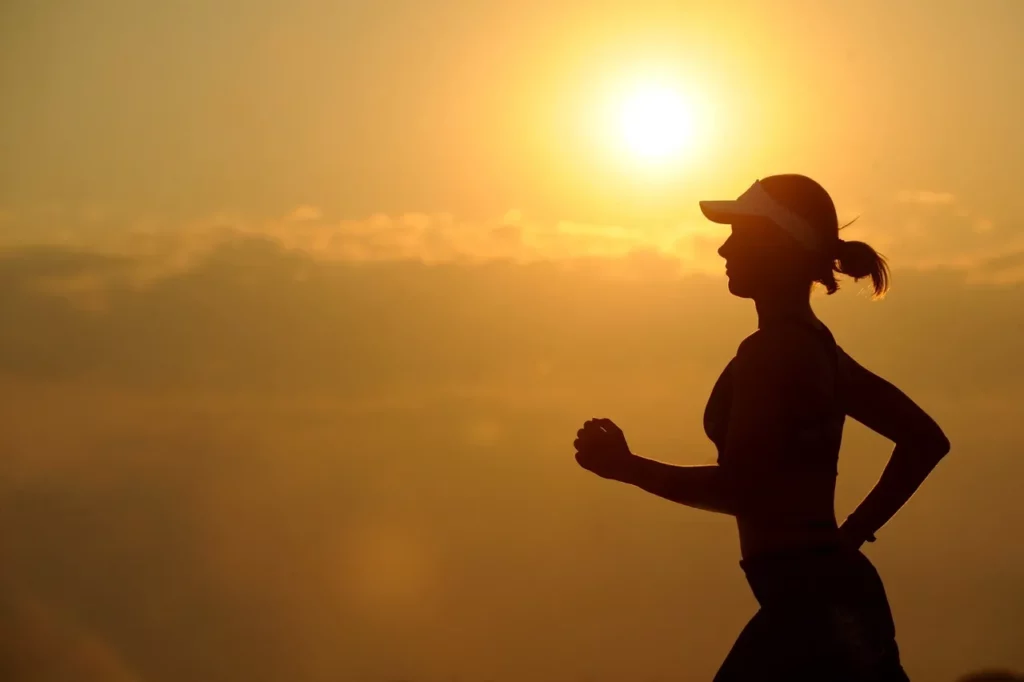 Silhouette of a person jogging at sunrise with a bright sun in the background.